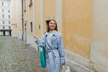 Photo for Overjoyed woman walking near weathered building with yellow wall on street in Vienna - Royalty Free Image
