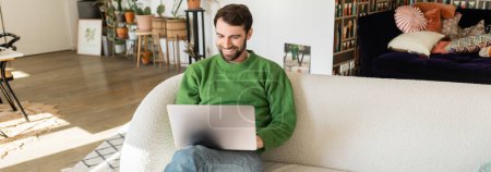 Joyeux brunette et pigiste barbu en pull vert et jeans travaillant sur ordinateur portable, bannière 