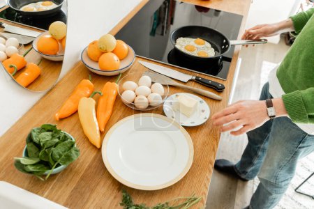 Téléchargez les photos : Vue recadrée de l'homme cuisinant des œufs près du beurre, des poivrons et des épinards sur le plan de travail dans la cuisine moderne - en image libre de droit