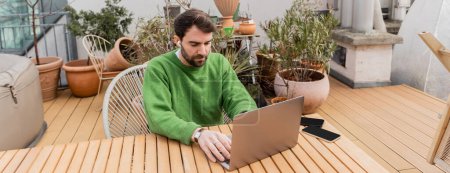 freelancer in earphone using laptop and working on rooftop terrace of house, banner 