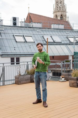 freelancer using earphones and smartphone and standing on rooftop terrace in Vienna 