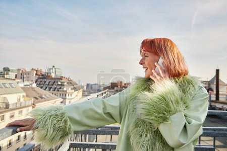 Trendfrau in stylischer Freizeitkleidung telefoniert auf Dachterrasse in Wien