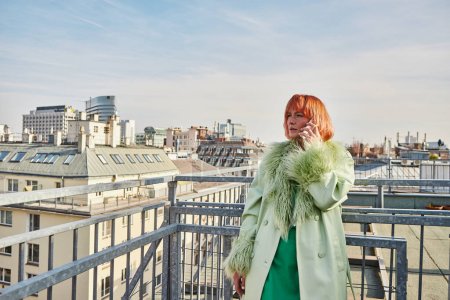 verführerische Frau in stylischer Freizeitkleidung, die auf der Dachterrasse in Wien mit dem Handy telefoniert