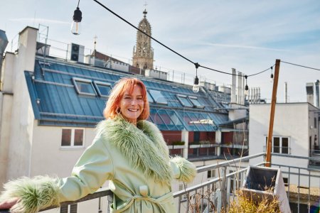 delighted woman in trendy casual attire looking at camera on roof terrace in Vienna, Austria