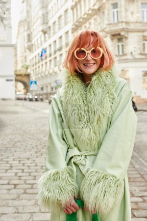 street fashion, joyful woman traveler in trendy sunglasses walking on city street in Vienna, Austria