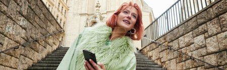 estilo de vida moderno, mujer elegante con teléfono móvil mirando hacia otro lado en la calle urbana de Viena, pancarta
