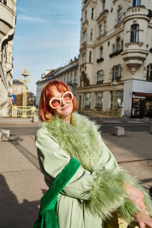 street fashion, pleased and fashionable woman in sunglasses smiling on urban street in Vienna