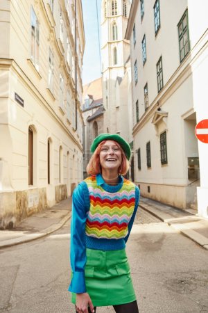 overjoyed woman in beret and trendy clothes laughing at camera on city street in Vienna, Austria