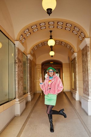 Téléchargez les photos : Femme excitée en tenue tendance et lunettes de soleil montrant signe de victoire dans la construction de Vienne, Autriche - en image libre de droit