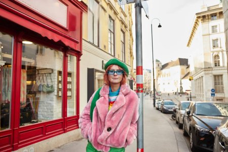 Téléchargez les photos : Femme à la mode en fausse fourrure veste et lunettes de soleil regardant caméra sur la rue de la ville à Vienne, Autriche - en image libre de droit