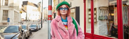 Téléchargez les photos : Femme élégante en fausse fourrure veste et lunettes de soleil regardant la caméra sur la rue de la ville à Vienne, bannière - en image libre de droit