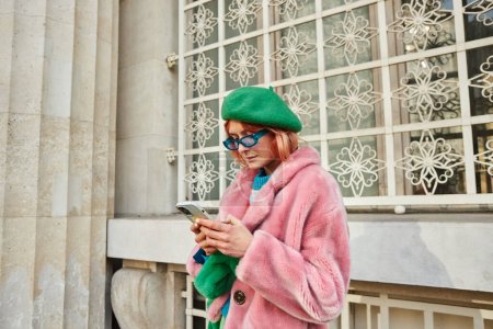 Téléchargez les photos : Femme en lunettes de soleil et veste en fausse fourrure à la mode avec smartphone dans la rue à Vienne, Autriche - en image libre de droit