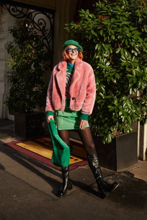 cheerful stylish woman in eyeglasses and faux fur jacket laughing on street in Vienna, Austria