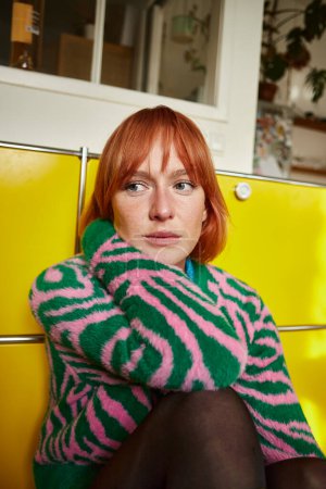 Nachdenkliche Frau im Animal-Print-Pullover sitzt in moderner Wohnung in Wien und schaut weg