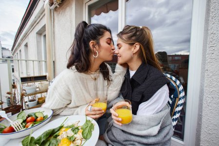 Foto de Joven lesbiana mujer besos nariz de su novia mientras desayunando en balcón, lgbt pareja - Imagen libre de derechos