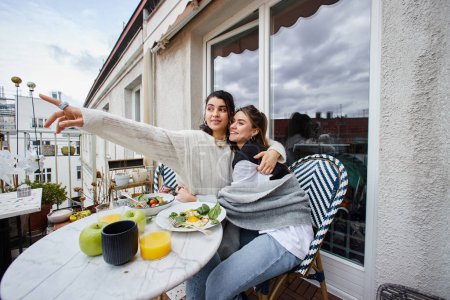 glücklicher Moment eines jungen lesbischen Paares, das sich beim Frühstück auf dem Balkon umarmt