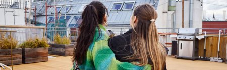 Tender moment between young lesbian couple sitting together on a rooftop, horizontal banner