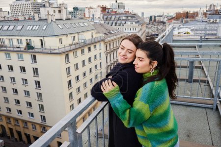 Téléchargez les photos : Jeune couple lesbien en tenue décontractée regardant la ville sur le toit, un moment d'amour et de connexion - en image libre de droit