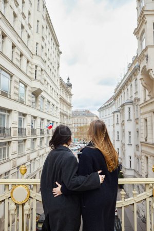 Intimes Moment auf dem Balkon mit Blick auf die Stadt als Hintergrund, Rückansicht lesbischer verliebter Frauen