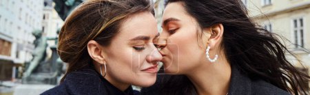 happy lesbian woman kissing in cheek her girlfriend by a fountain statue in Vienna, banner