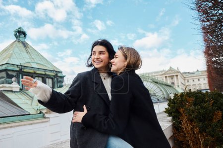 Photo for Cheerful lesbian couple in outerwear smiling while spending time together near building in Vienna - Royalty Free Image
