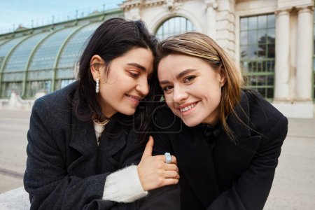 portrait of happy lesbian woman embracing her girlfriend near Palmenhaus in Vienna on background