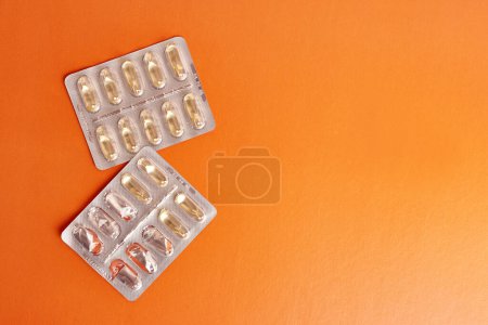 Foto de Vitaminas en forma de cápsulas sobre fondo naranja. Tratamiento y prevención de enfermedades. Fortalecimiento de la inmunidad. - Imagen libre de derechos