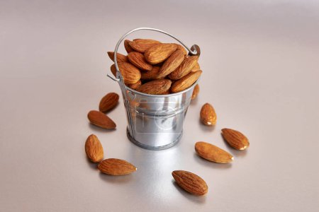 A small metal bucket filled with dried almond kernels on a gray background.