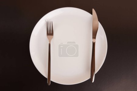 Téléchargez les photos : Plaque blanche avec fourchette et couteau sur fond noir. - en image libre de droit