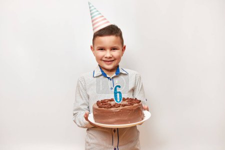 Fröhlicher Junge mit einer Geburtstagstorte und einer Kerze in Form der Zahl 6. Konzept zur Geburtstagsfeier.