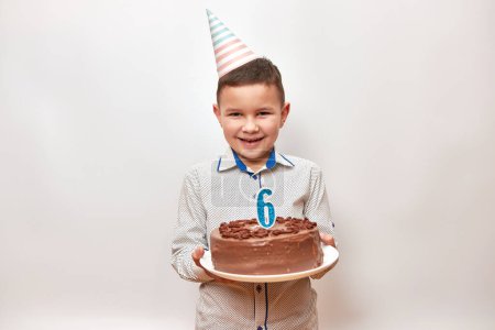 Photo for Cheerful boy holding a birthday cake with a candle in the form of number 6. Birthday celebration concept. - Royalty Free Image