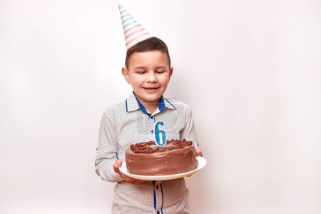 Cheerful boy holding a birthday cake with a candle in the form of number 6. Birthday celebration concept.