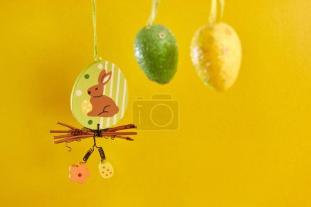 Photo for Easter beauty with a hanging rabbit and eggs on a yellow background. Easter celebration. - Royalty Free Image