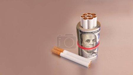 Photo for Cigarettes wrapped in 100 dollar bills on a gray background. The concept of a constant increase in the price of cigarettes. - Royalty Free Image