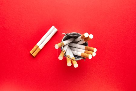 Photo for A small metal bucket filled with cigarettes on a red background. View from above. - Royalty Free Image