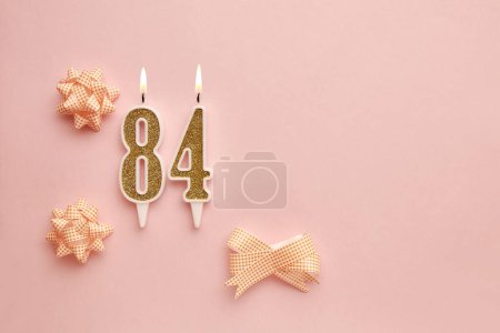 Candles with the number 84 on a pastel pink background with festive decor. Happy birthday candles. The concept of celebrating a birthday, anniversary, important date, holiday. Copy space. banner