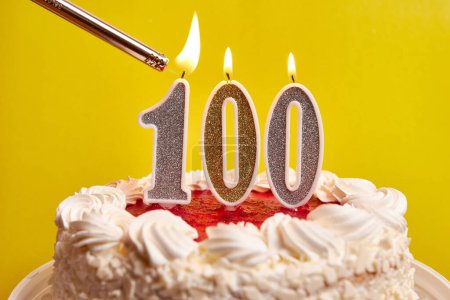 Téléchargez les photos : Une bougie sous la forme du numéro 100 est allumée, coincée dans un gâteau de vacances. Célébrer un anniversaire ou un événement marquant. Le point culminant de la célébration. - en image libre de droit