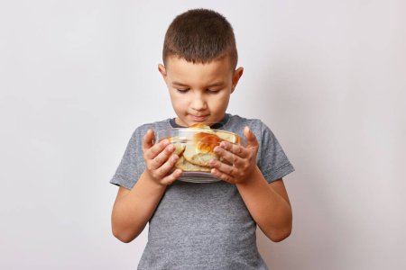 Téléchargez les photos : Un garçon souriant tient un bol de tartes au brownie fraîches, fraîches du four. Délicieux dessert maison. - en image libre de droit