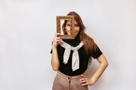 A beautiful girl poses for the camera, looking into a photo frame.