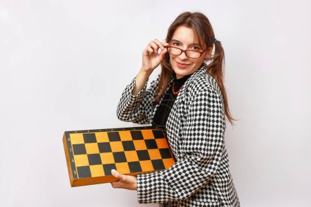 Cheerful female student in glasses holds chess in her hands.