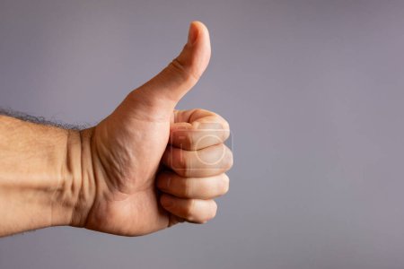 Human hand showing thumb up (like) gesture on gray background.