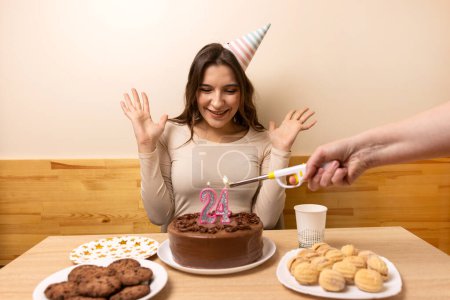 Una niña está sentada frente a una mesa con un pastel festivo, en el que se enciende una vela en forma de número 24. El concepto de una celebración de cumpleaños.