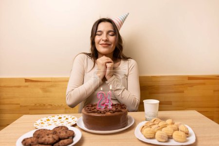 Foto de Una niña está sentada frente a una mesa con un pastel festivo, en el que se enciende una vela en forma de número 24. El concepto de una celebración de cumpleaños. - Imagen libre de derechos
