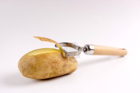 Peeled raw potato and shell and knife for peeling on white background.