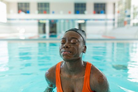 Photo for Black young woman with water flowing over her skin at the heated swimming pool during a winter day - Royalty Free Image