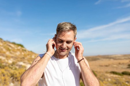 Téléchargez les photos : Un homme aux cheveux gris écoute de la musique avec des écouteurs lors d'une promenade à la campagne pour mener un mode de vie sain - en image libre de droit