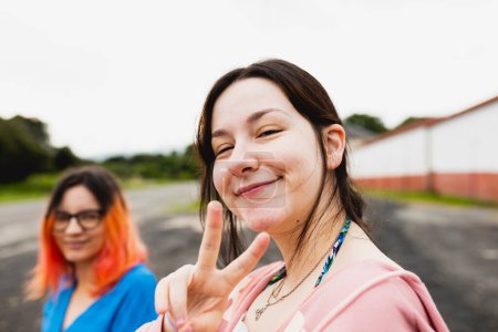 Téléchargez les photos : Une jeune femme fait le geste du signe V avec ses doigts alors qu'elle passe un moment joyeux avec son amie lors d'un arrêt de voiture - en image libre de droit