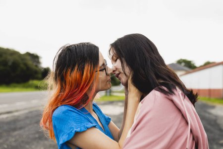 Téléchargez les photos : Un couple de jeunes lesbiennes amoureuses, en voyage, l'une d'elles aux cheveux teints à l'orange, s'embrasse passionnément et amoureusement - en image libre de droit