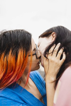 Téléchargez les photos : Un couple de jeunes lesbiennes amoureuses, en voyage, l'une d'elles aux cheveux teints à l'orange, s'embrasse passionnément et amoureusement - en image libre de droit