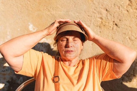 Foto de Una mujer jubilada ajusta su gorra para protegerse del sol mientras disfruta de la tarde sentada fuera de un bar en la calle, Galicia, España - Imagen libre de derechos